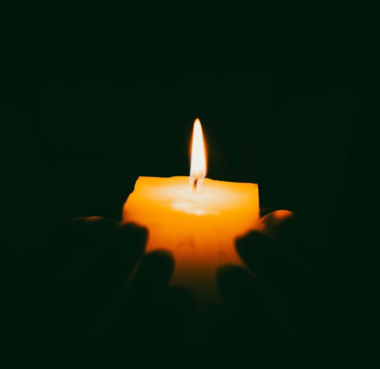 A close-up of hands holding a candle, providing soft illumination in darkness.