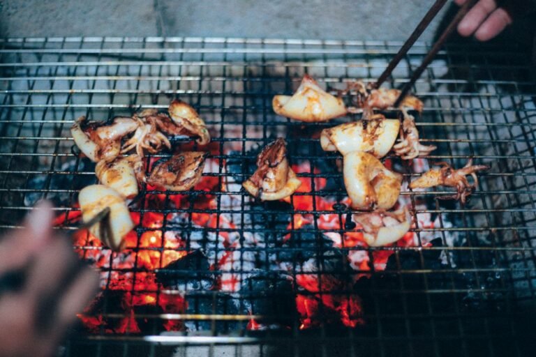 Close-up of delicious grilled squid on a barbecue grill in Phú Quốc, Vietnam, featuring vibrant coals and chopsticks.