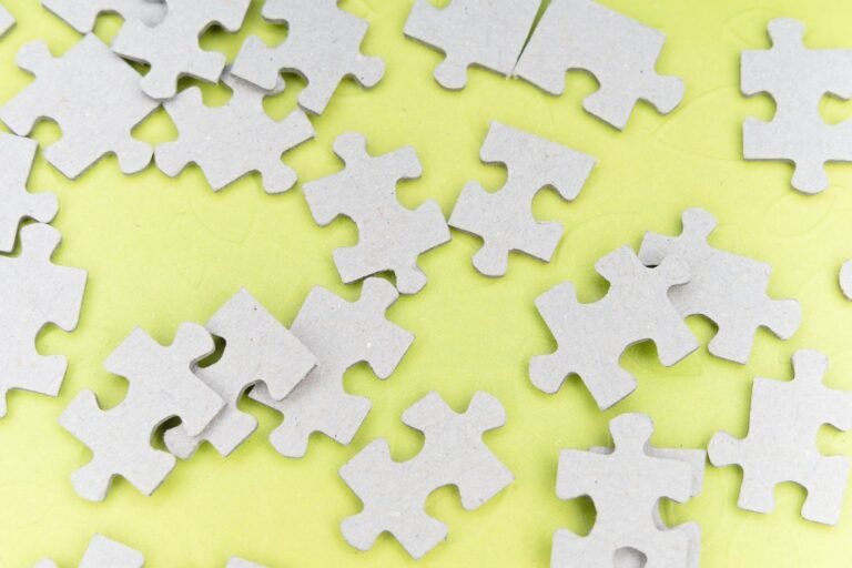 Close-up of gray puzzle pieces scattered on a vibrant yellow background for a playful abstract composition.