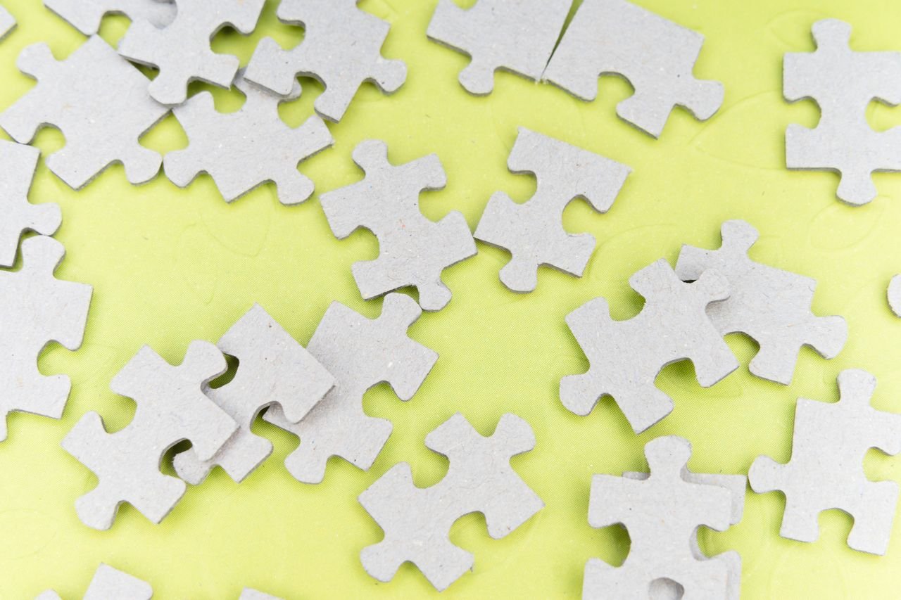 Close-up of gray puzzle pieces scattered on a vibrant yellow background for a playful abstract composition.