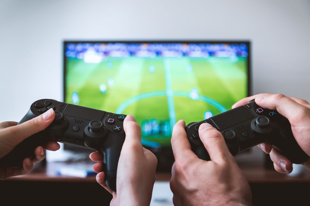 Hands holding gaming controllers in front of a TV, illustrating the multiplayer gaming experience of Steal a Brainrot .io
