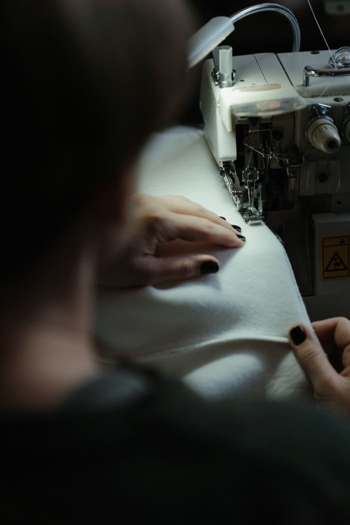 Focused seamstress using sewing machine for fabric stitching indoors.