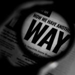 Black and white close-up of newspaper text magnified through a lens, emphasizing the word 'WAY'.
