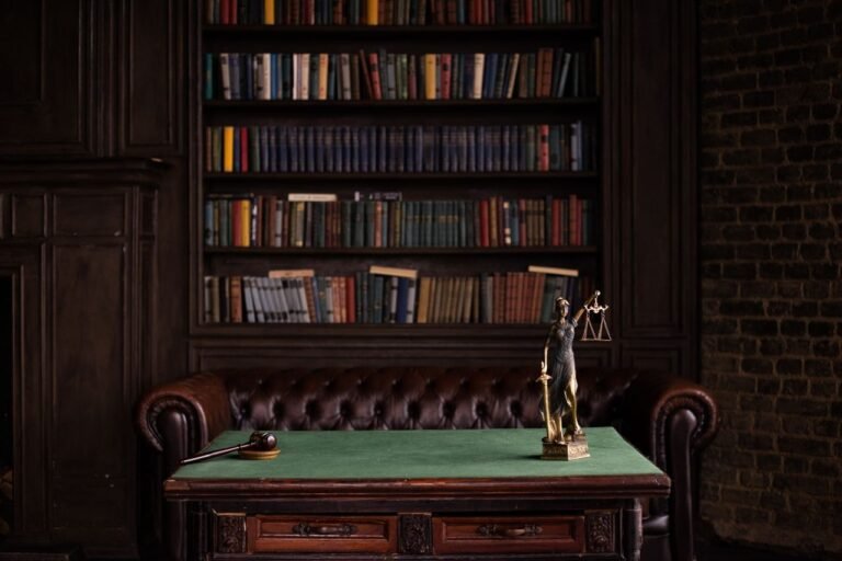 A classic study room with shelves of books, a gavel, and Lady Justice figurine on a green table.