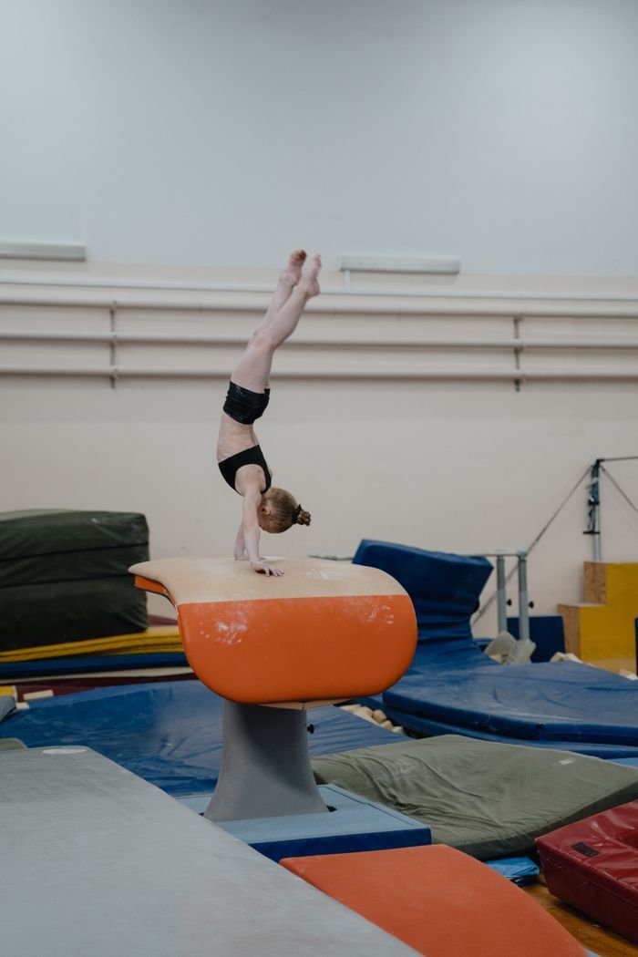 A young gymnast skillfully balances in a handstand on a vault indoors.
