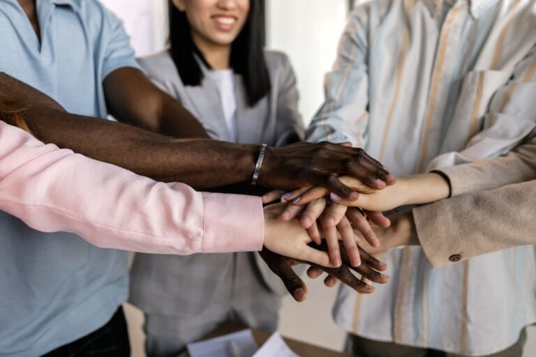 Diverse hands stacked in unity -- people over papers philosophy, valuing humanity over credentials