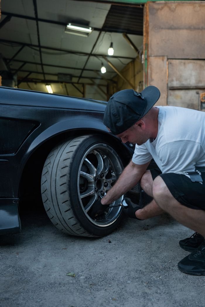 A man changes a car tire in a garage workshop, showcasing automotive maintenance.