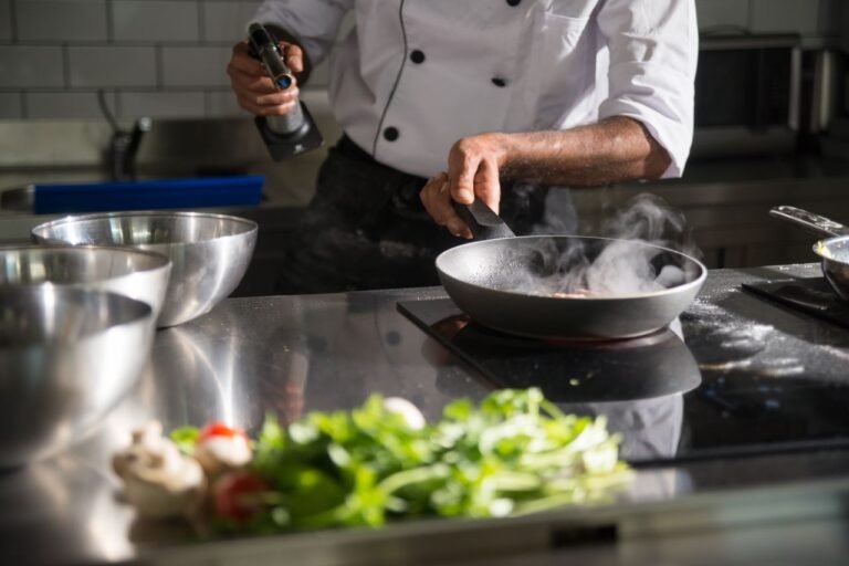 Chef prepares food in a sleek kitchen using a frying pan on an induction cooktop.