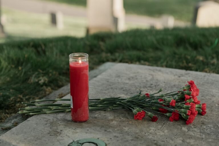 A red candle and carnations resting on a grave, symbolizing remembrance and tribute.